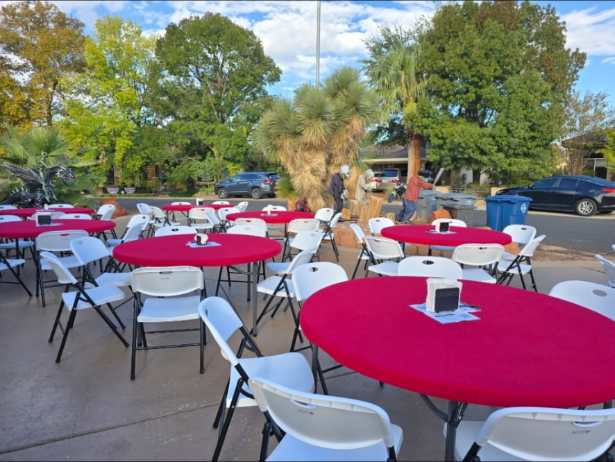 Outdoor breakfast tables with red tablecloths and white chairs set for neighbors.