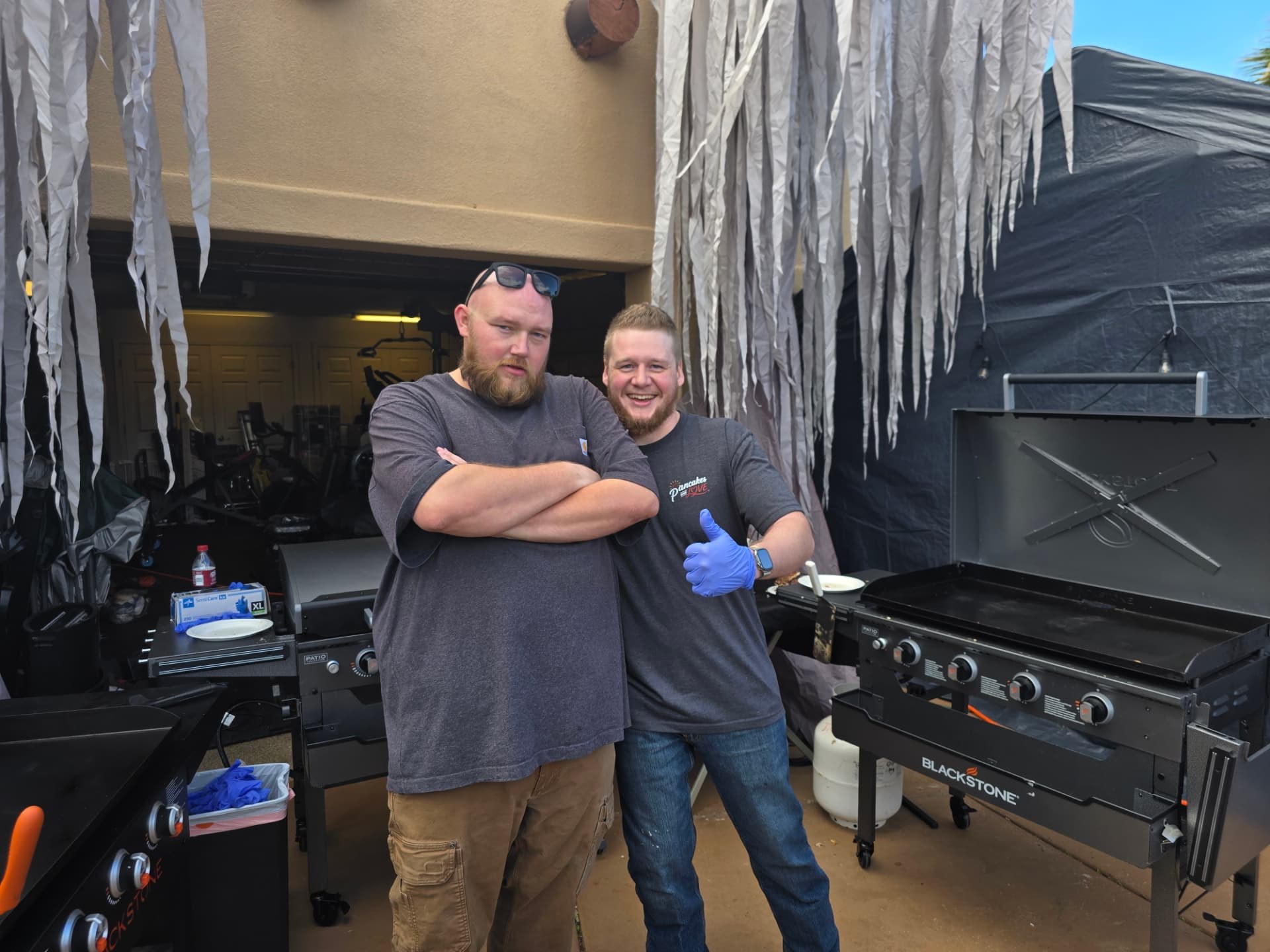 Two volunteers smiling and giving a thumbs-up by the griddles.