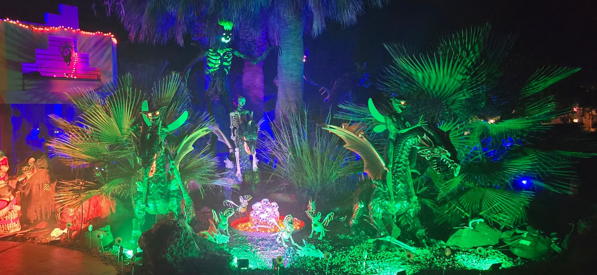 Halloween decorations illuminated with colorful lights among palm trees.