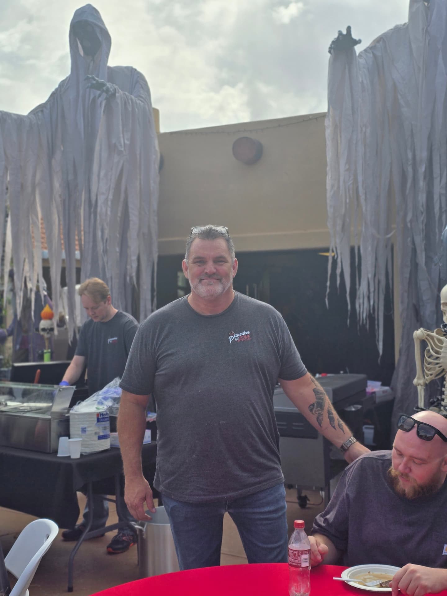 A volunteer smiling among the breakfast tables and Halloween decorations.