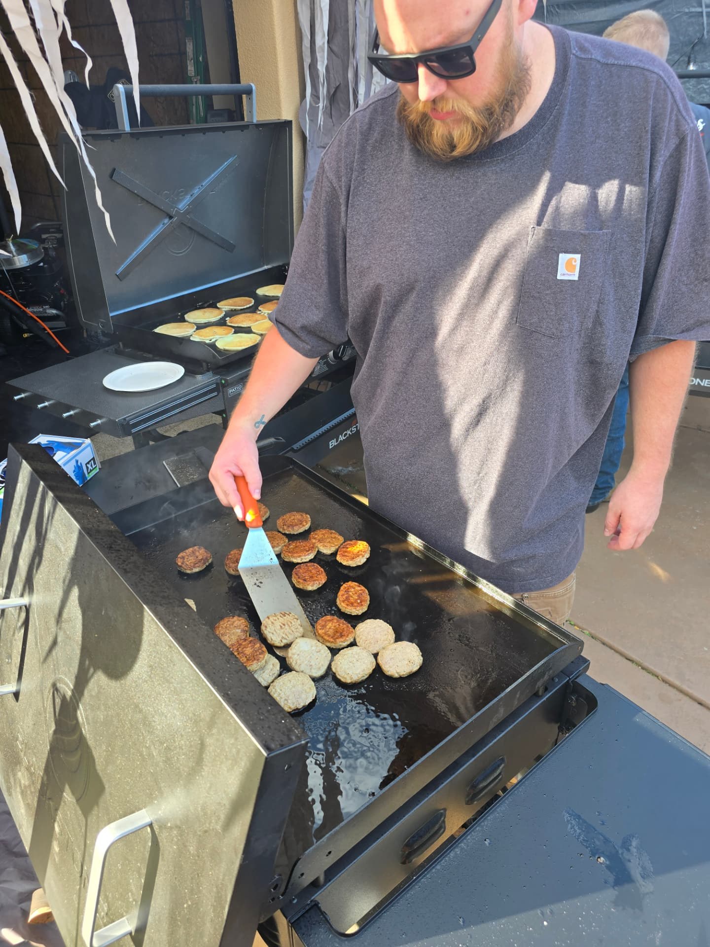 A volunteer cooking sausage on the griddle.