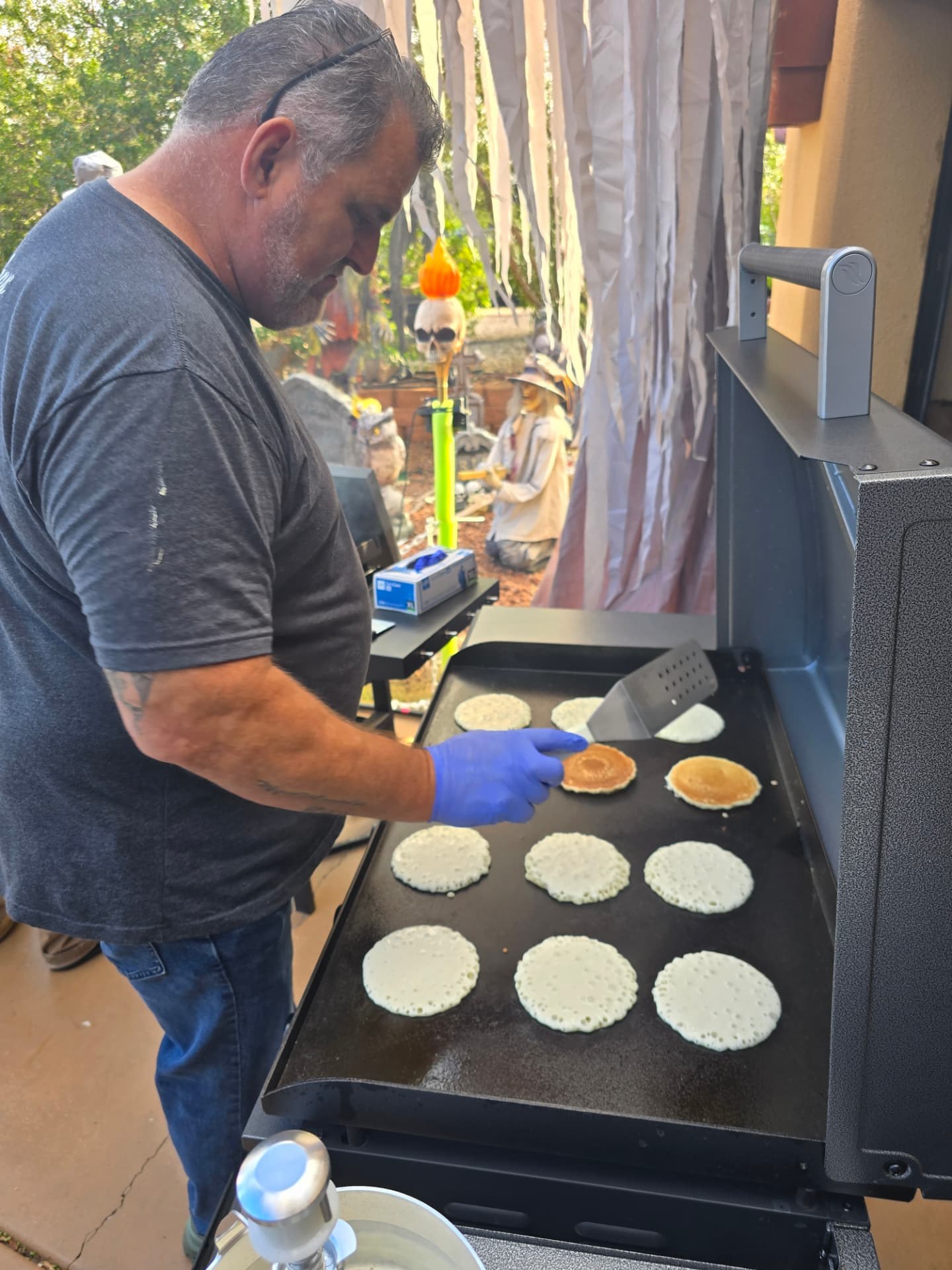 A volunteer pouring pancakes on a full griddle.