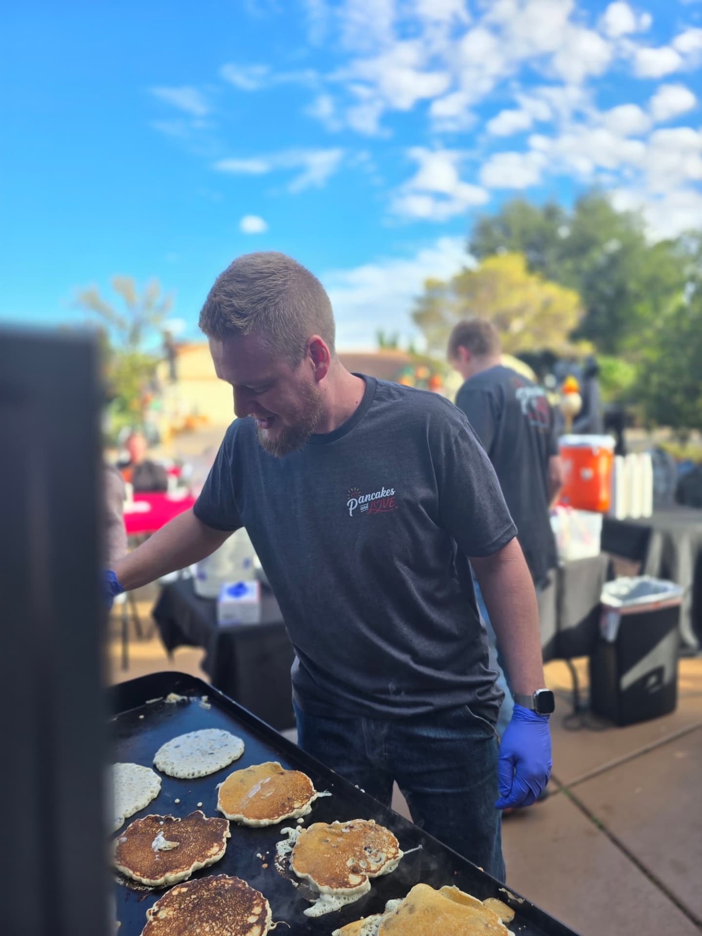 A volunteer cooking pancakes on the griddle under a blue sky.